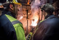 Silhouette of workers looking on as molten metal is poured in foundry — Stock Photo
