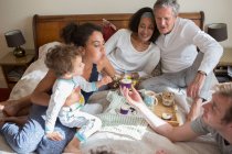 Famille de trois générations assise sur le lit, soufflant la bougie sur le cupcake — Photo de stock