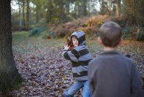 Niño lanzando hojas a amigo en bosques otoñales - foto de stock