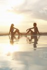 Пара сидящих на бесконечности у бассейна при солнечном свете — стоковое фото
