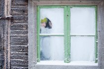 Woman peering out frosty window — Stock Photo