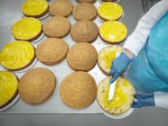 Imagen recortada de panadero femenino esparciendo relleno en pasteles en la fábrica de pasteles - foto de stock