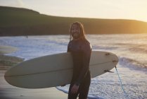Retrato de un joven surfista que lleva tabla de surf en la playa, Devon, Inglaterra, Reino Unido - foto de stock