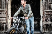 Junger Mann schubst Motorrad aus Scheune — Stockfoto