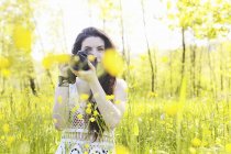 Jovem mulher segurando câmera no campo florido — Fotografia de Stock