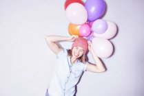 Studioaufnahme einer jungen Frau mit einem Bündel Luftballons auf dem Kopf — Stockfoto