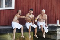 Троє чоловіків сидять з пивом поза сауною — стокове фото