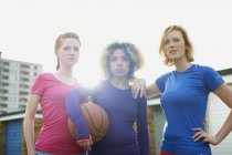 Retrato de tres mujeres ejercitándose juntas sosteniendo una pelota de baloncesto - foto de stock