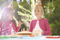 Chicas con dedo en la torta de cumpleaños en la fiesta de cumpleaños jardín - foto de stock