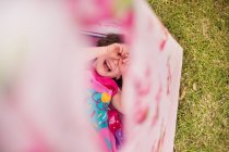 Overhead view of girl in teepee, hands covering eyes smiling — Stock Photo