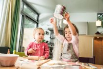 Girl sieving flour in kitchen — Stock Photo