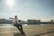 Geschäftsmann sitzt mit Tablet auf Stuhl auf Straßenbahngleisen — Stockfoto