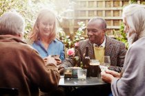 Senior friends drinking and playing cards in garden — Stock Photo