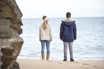 Vista trasera de una pareja joven mirando desde la playa, Constantine Bay, Cornwall, Reino Unido - foto de stock