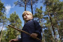 Хлопчик стоїть в лісі тримає палицю — стокове фото