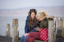 Ragazze adolescenti sedute sul molo e ascoltare musica — Foto stock