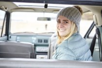 Portrait de jeune femme en voiture à la plage portant un chapeau en tricot — Photo de stock