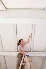 Женщина на стремянках, рисующая белый потолок — стоковое фото