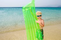 Jeune garçon tenant matelas gonflable à la plage — Photo de stock