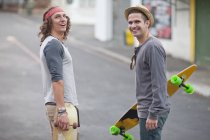 Portrait of two male adult friends with skateboards on city street — Stock Photo