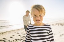 Портрет хлопчика на пляжі з батьком, дивлячись на камеру посміхаючись — стокове фото