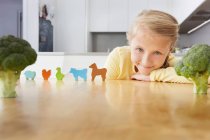Menina brincando com animais de brinquedo em torno de brócolis — Fotografia de Stock