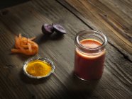 Suco cru de laranja em um jarro com beterraba, açafrão e cenoura ralada em madeira — Fotografia de Stock