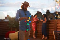 Man hanging garden lights for early evening party — Stock Photo