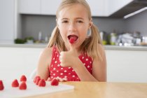 Girl eating raspberry from thumb — Stock Photo
