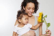 Baby berührt Sonnenblume, die von Mutter im Studio gehalten wird — Stockfoto