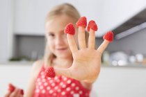 Chica poniendo frambuesas en los dedos - foto de stock