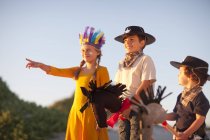 Three children dressed as native american and cowboys pointing from sand dunes — Stock Photo