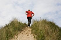 Rear view of man running up grassy hillside — Stock Photo