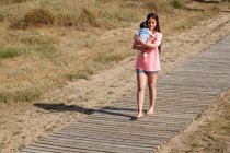 Mutter läuft mit Baby im Arm über Strandpromenade — Stockfoto