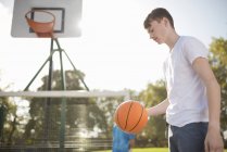 Joven jugador de baloncesto masculino en cancha con baloncesto - foto de stock