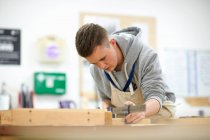 Мужчина, занимающийся плотничеством, настраивает деревянный зажим в мастерской колледжа — стоковое фото