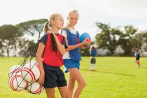 Chica llevando pelotas de fútbol en el campo - foto de stock