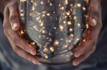 Cropped view of hands holding glass jar filled with decorative lights — Stock Photo