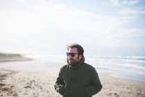 Hombre adulto medio con las manos en el bolsillo en la playa ventosa, Sorso, Sassari, Cerdeña, Italia - foto de stock