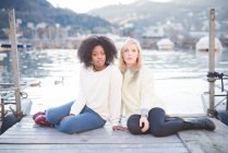 Portrait of two female friends sitting on pier, Lake Como, Italy — Stock Photo
