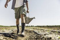Грудь человека в грязном поле, несущего банку с водой — стоковое фото
