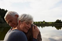 Старшая пара обнимается перед озером — стоковое фото
