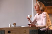 Femme âgée tenant tasse de café et téléphone mobile — Photo de stock