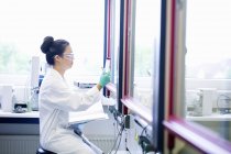 Молодая женщина-ученый с блокнотом смотрит на образец в лаборатории — стоковое фото
