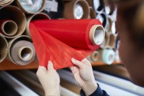 Mani di lavoratrice esaminando tessuto rosso per tende a rullo in fabbrica — Foto stock