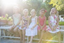 Retrato de cinco niñas sentadas en el banco del jardín - foto de stock
