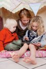 Children using tablet computer in fort — Stock Photo