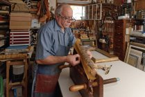 Старший чоловік ремонтує крихкий антикварний книжковий хребет у традиційній книжковій майстерні — стокове фото