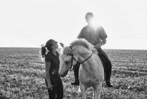B&W image of woman chatting with man riding grey horse in field — Stock Photo