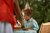 Mère avec fils soufflant des bougies sur le gâteau d'anniversaire à la fête d'anniversaire du jardin — Photo de stock